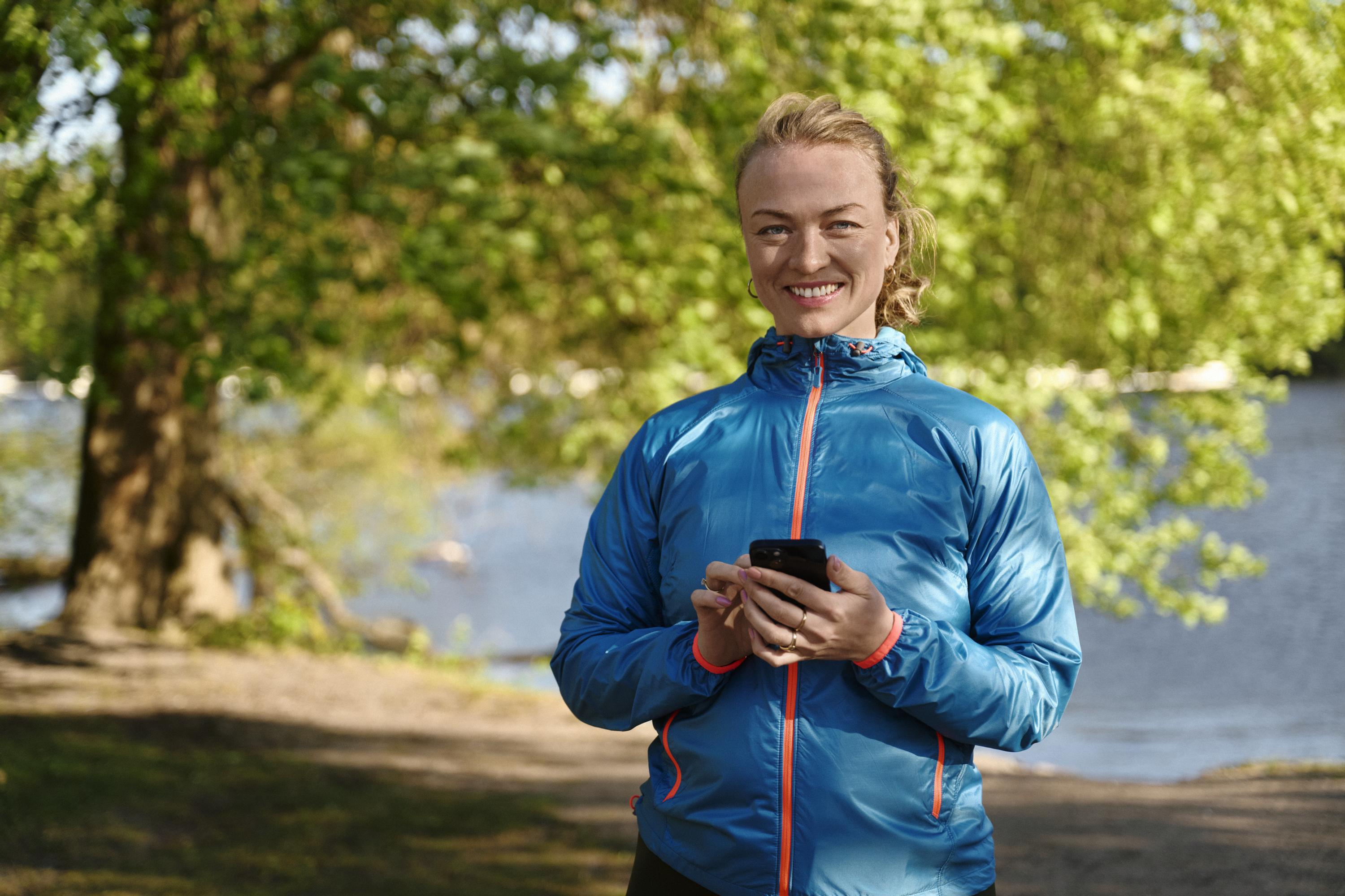 Träningsklädd kvinna står och håller i en mobiltelefon