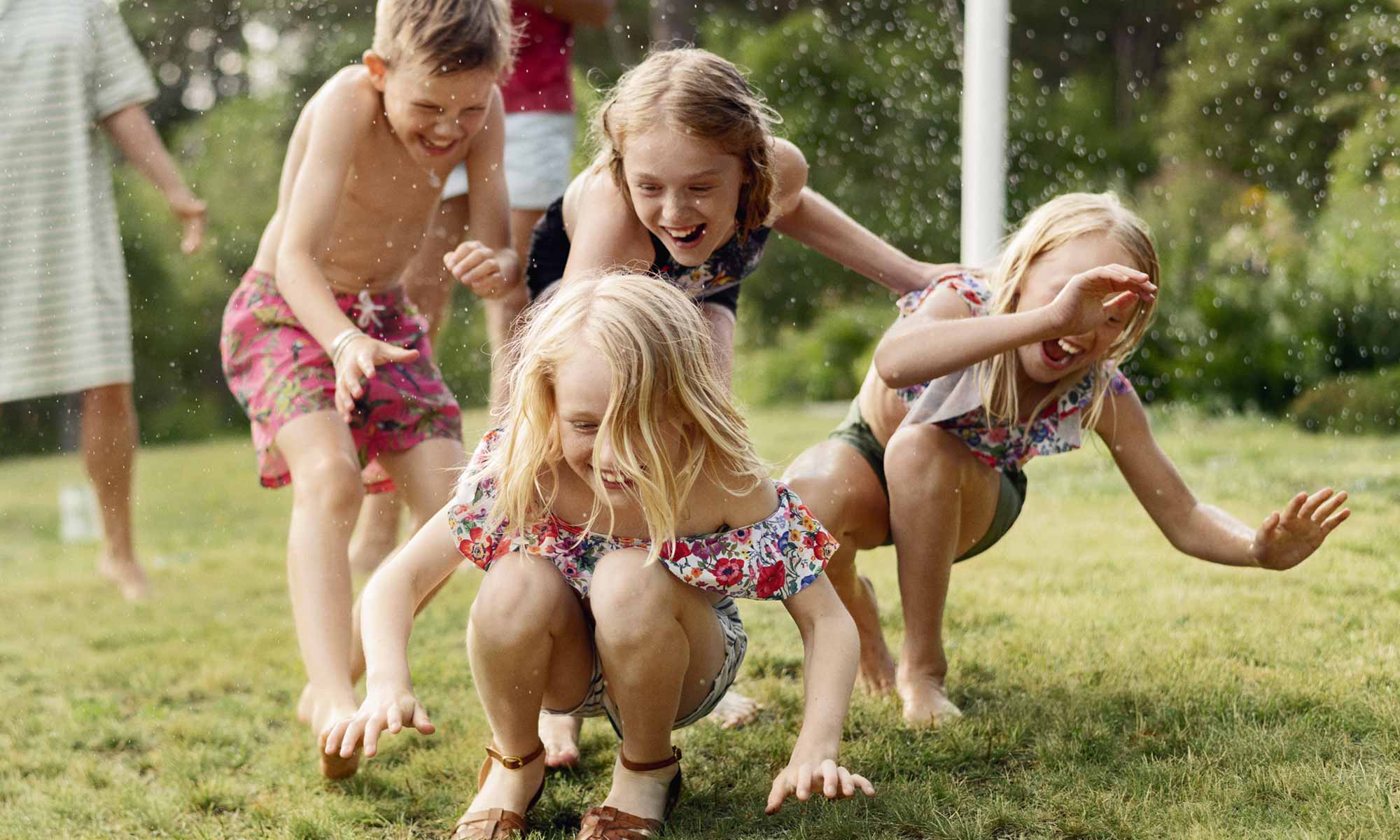 Skrattande barn leker ute i trädgården med en vattenspridare en solig sommardag