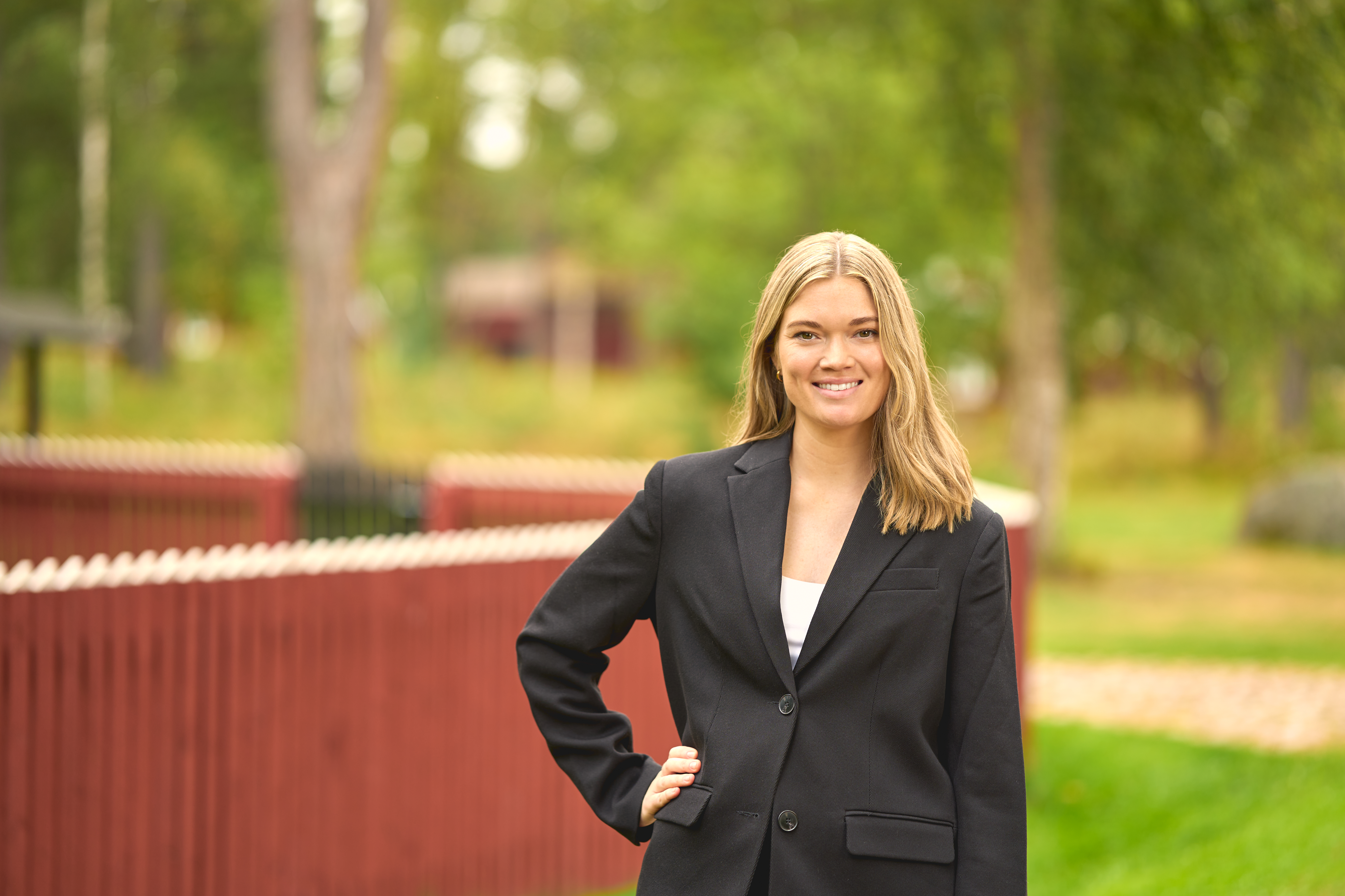 Leende kvinna står framför ett rött staket och gröna träd