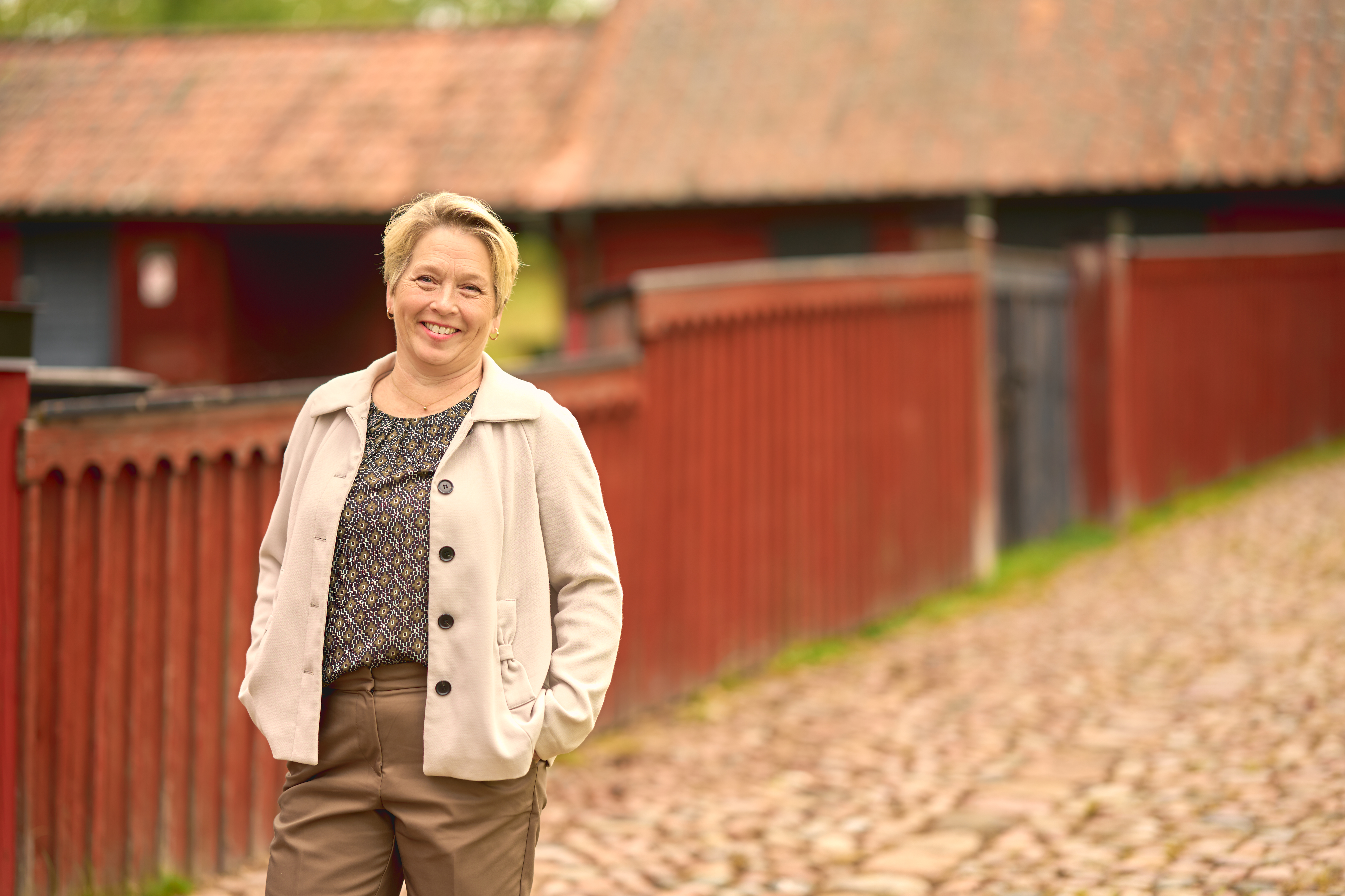 Leende kvinna står framför ett rött staket och röda hus