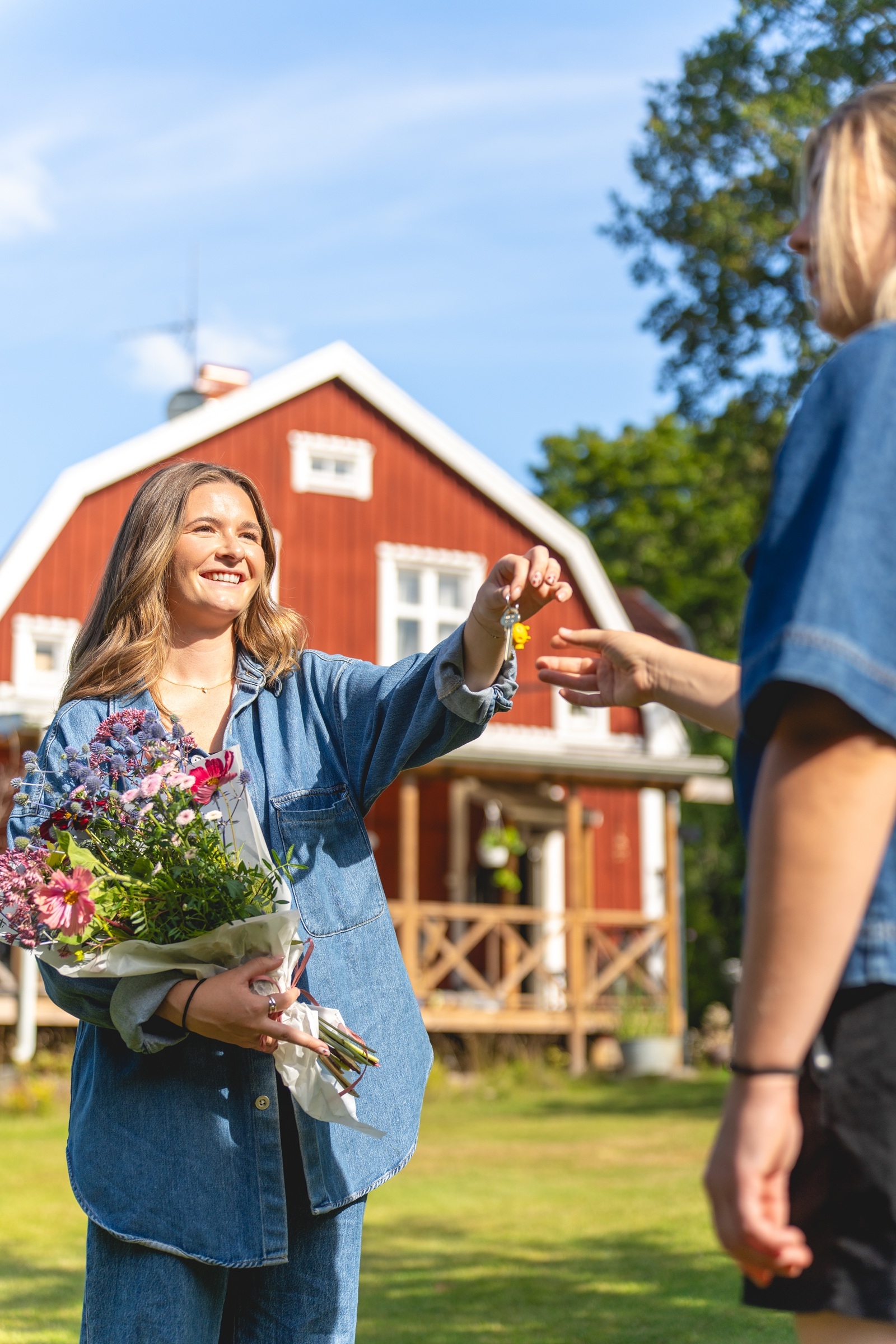 En kvinna håller i en blombukett och ger nycklar till en annan kvinna